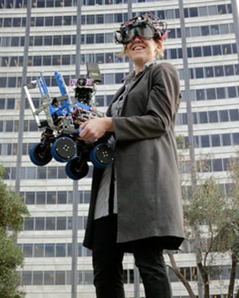 A woman holding a robot in front of a building.