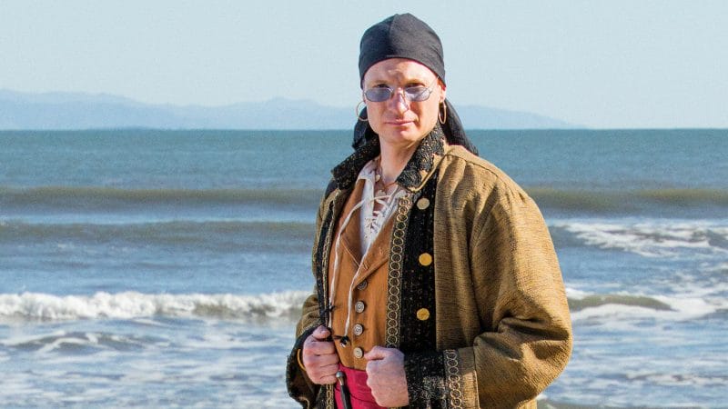 A man in a pirate costume reenacting pirate history on the beach.