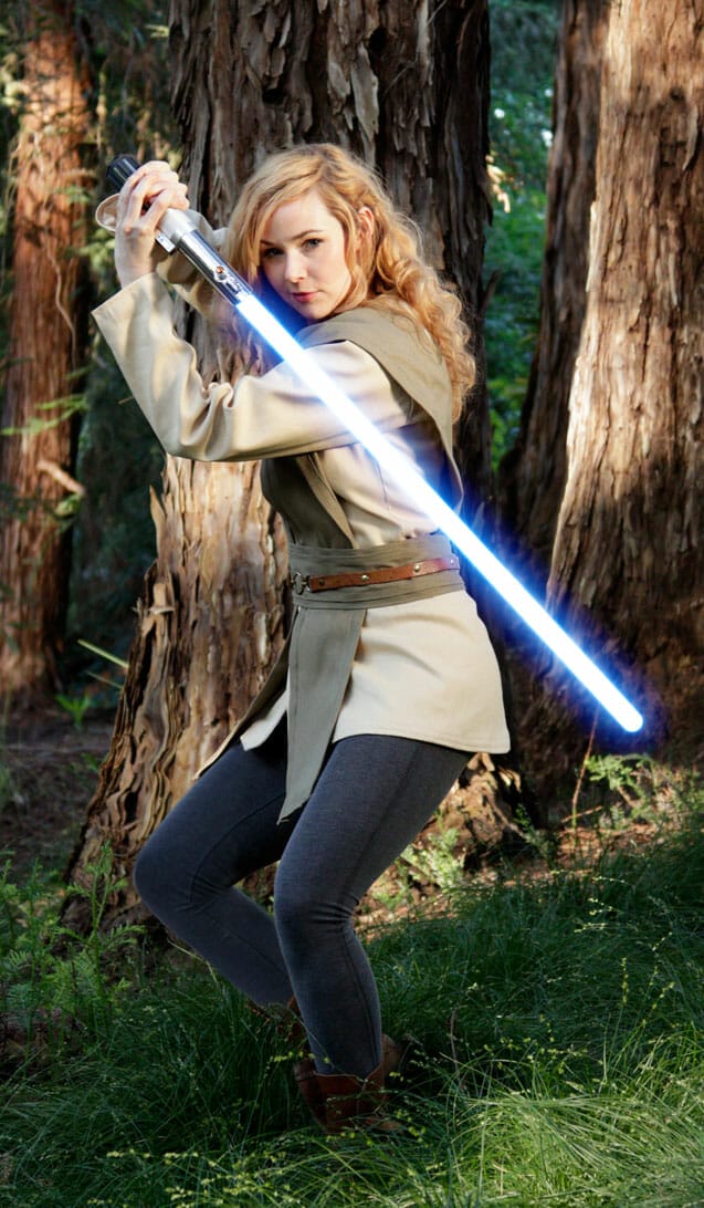 A woman holding a star wars saber in the woods.