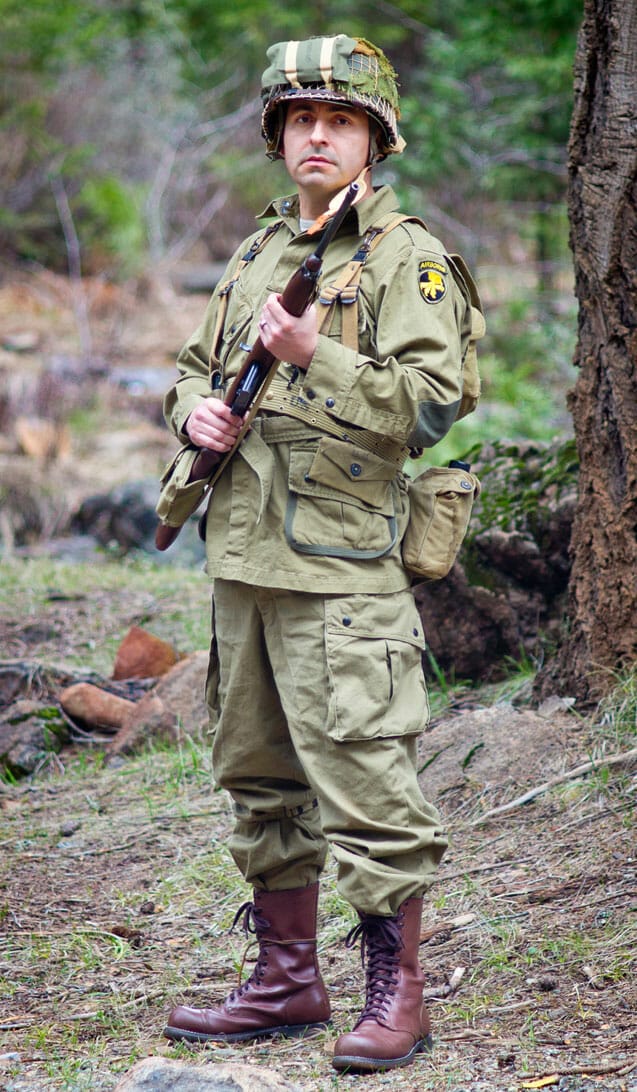 A man in a military uniform holding a rifle in the woods.