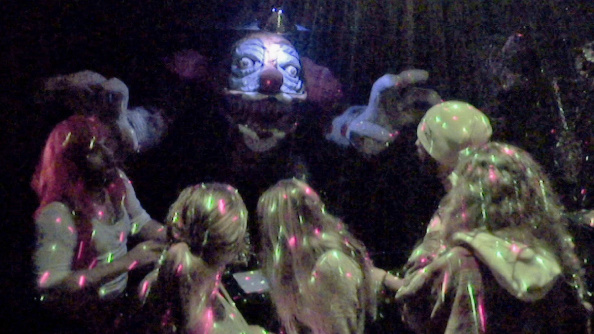 A group of people standing around a clown in a dark room.