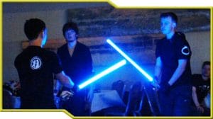 Two Star Wars fans wielding blue lightsabers at a party.