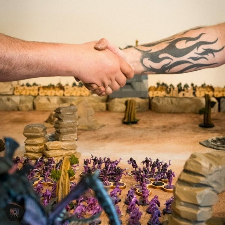 Two men shaking hands in front of a table with miniature figures.