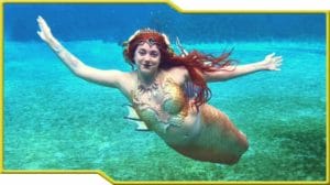 A woman in a mermaid costume is swimming in the ocean as a mermaid.