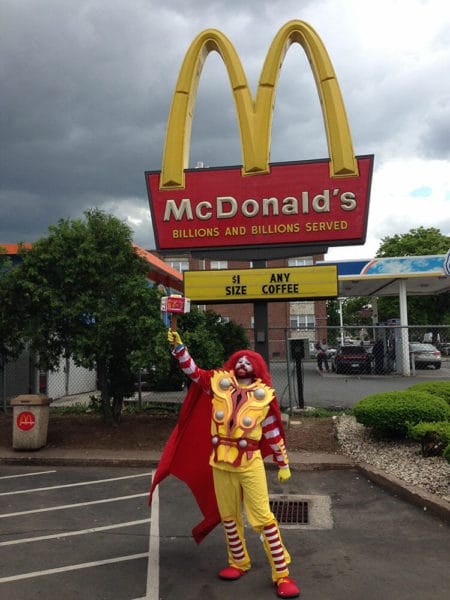 A man dressed as a mcdonald's clown standing in front of a mcdonald's.