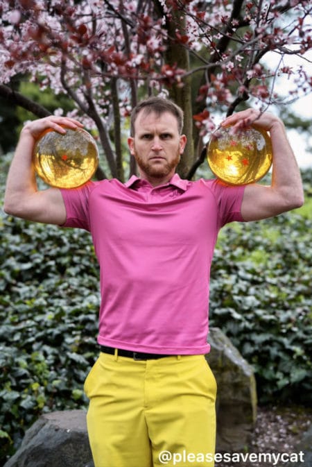 A man in a pink shirt and yellow pants holding two gold balls.