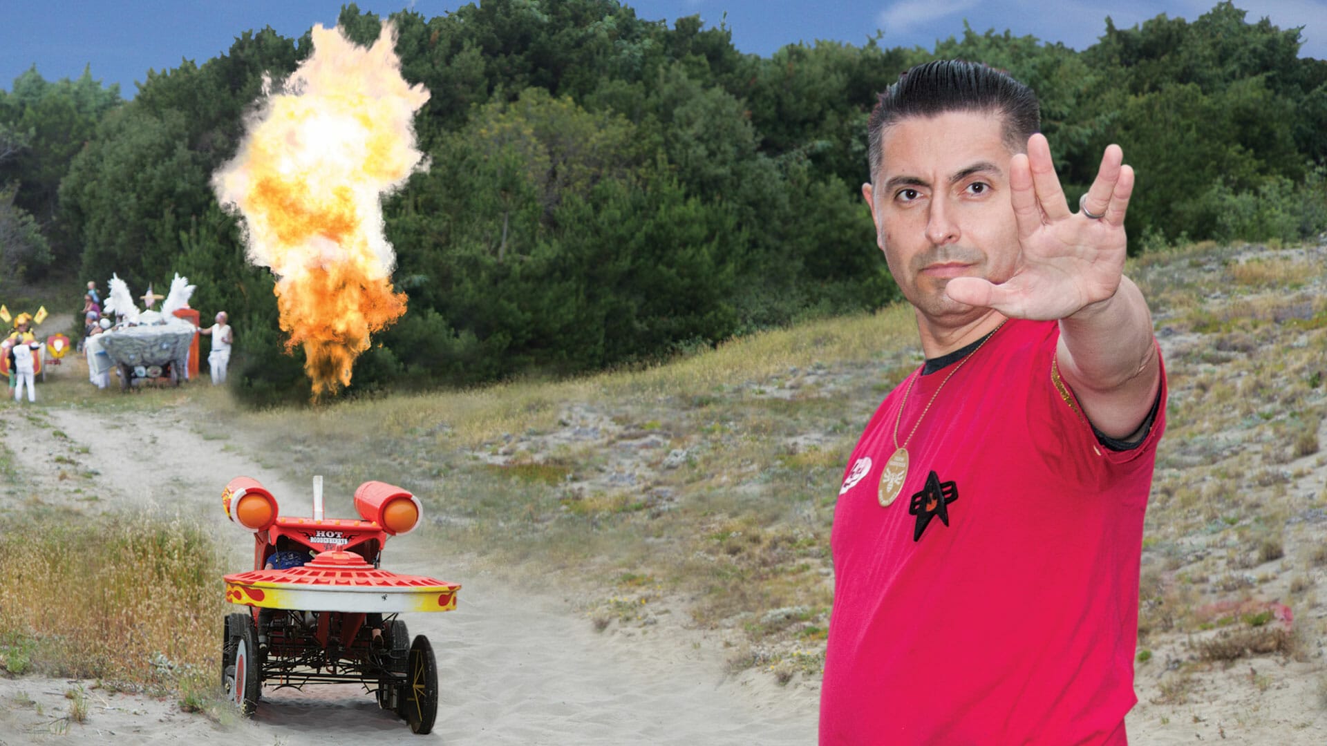 A man in a red shirt is standing next to a fire truck at the Kinetic Sculpture Racing event.