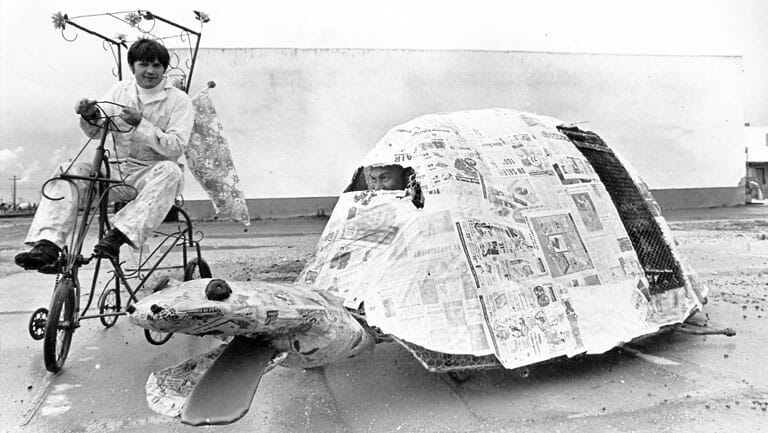A man on a bicycle next to a paper turtle.