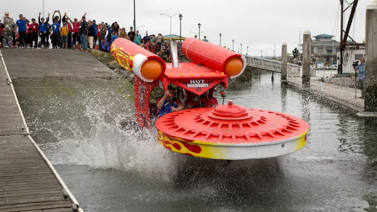 A red and yellow boat driving down a canal with people watching.