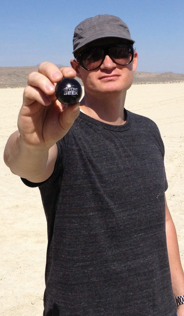 A man holding a black ball in the desert.